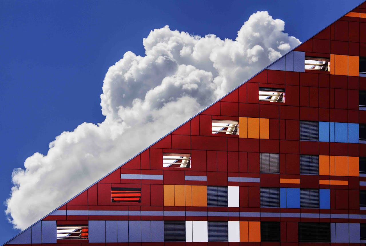 Colorful modern building facade against a backdrop of dramatic clouds and bright blue sky.
